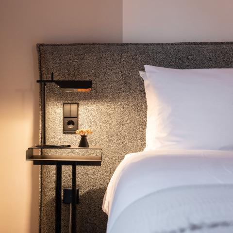 Gemütliches Hotelbett mit warmen Licht am Beistelltisch