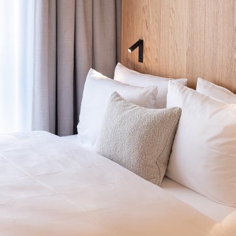 Hotel bed with pillows in front of a wooden wall