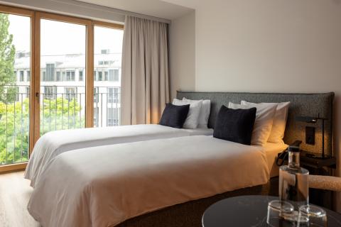 Large double bed in a bright hotel room with large windows