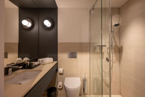 Badezimmer mit Duschkabine und Waschbecken vor einem großen Spiegel