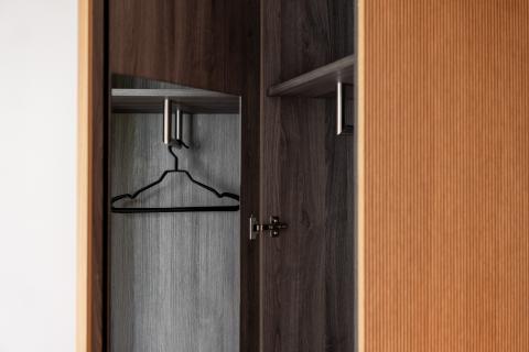 Ein leerer Kleiderbügel hängt in einem dunklen Keiderschrank mit einer braunen Tür