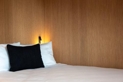 Hotelbett mit Kissen neben einer Holzwand