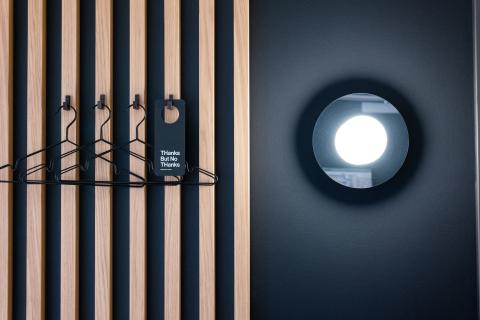 Black hangers hang on hooks in front of wooden wall next to round lamp