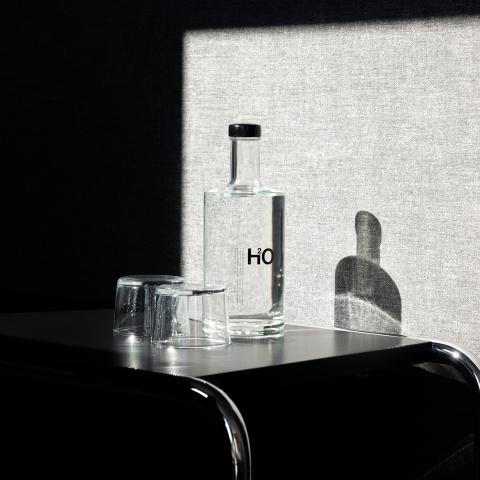A bottle of water and two glasses throwing a shadow at a grey wall