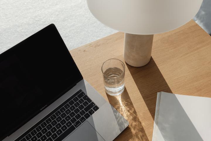 Arbeitsplatz mit einem Laptop, einem Wasserglas und einer weißen Lampe