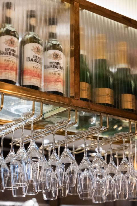 Wein und Sektflaschen stehen aufgereiht mit hängenden Gläsern in einem Regal des Boutique Hotels