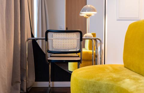 Ein kleiner Schreibtisch mit Tischlampe und ein gelbes Samt Sofa im Hotel in Schwabing