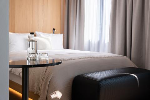 Hotelbett mit einem schwarzen Beistelltisch und einer Wasserflasche