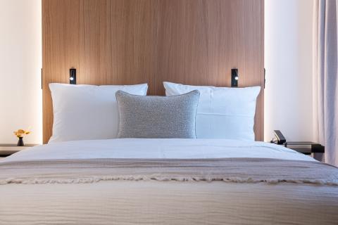 Großes Doppelbett mit aufgestellten Kissen vor einer beleuchteten Holzwand