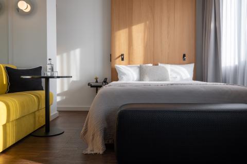 Rays of light fall into a modern hotel room with a double bed and a yellow sofa