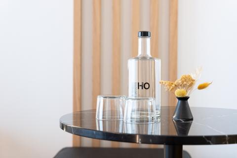 Eine Wasserflasche, zwei Gläser und Dekoblumen stehen auf einem schwarzen Marmortisch