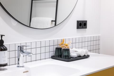 Im Badezimmer eines Hotels steht ein Waschbecken mit eingerollten Handtüchern und einem großen runden Spiegel