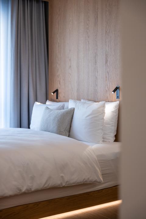 Headboard of hotel bed with two reading lamps and many pillows placed on it