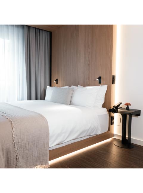 Ein schlichtes Hotelzimmer mit beleuchtetem Doppelbett, dezenten Farben und Holzelementen