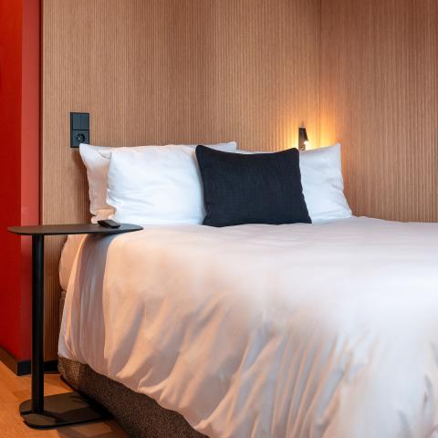 Hotel bed with pillows next to a lighted wooden wall